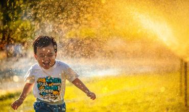 The Hidden Costs of Buying Your First Home A little boy running through the sprinklers on a sunny day