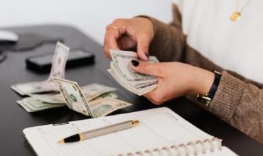 A person counting money on a desk with a notepad in front of them