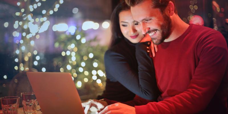 Things to Consider Before Entering the Housing Market Couple looking at computer screen, with Christmas tree in background