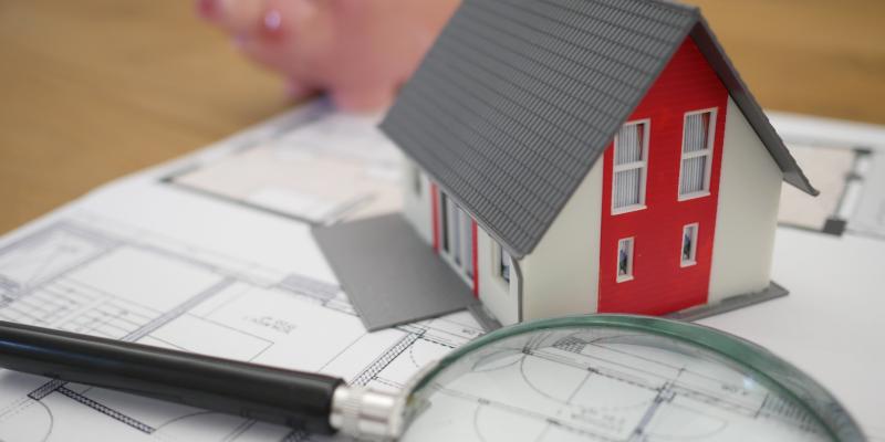 Buying a Home in 2020? Here’s What You Should Know A small red house sitting on blueprints next to a microscope and a piggy bank