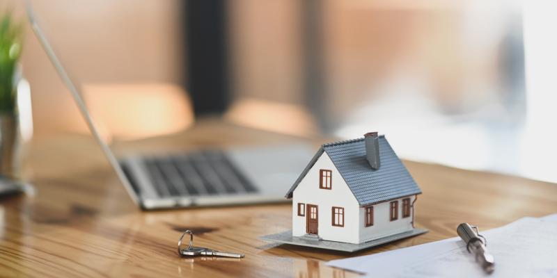 Impact investing preserves affordable housing, offers returns for investors Miniature house beside a keyboard and paperwork on desk