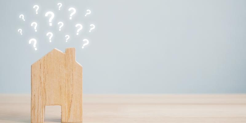 The Truth Behind 3 Common Home Buying Myths Small wooden house sitting on a desk with little question marks coming out of the roof