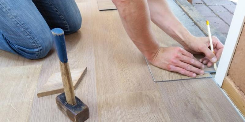A person fixing a door on their hands and knees with a hammer next to them